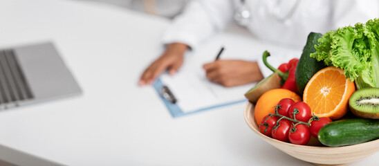 Close up of bowl of fresh fruits and vegetables on dietologist workplace, doctor making prescription