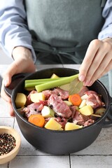 Wall Mural - Woman preparing stew with vegetables and meat at white tiled table, closeup