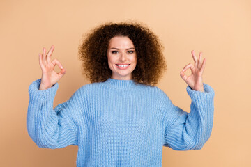 Sticker - Portrait of young charming beautiful curly haired lady in blue fall season sweater showing okey sign isolated on beige color background