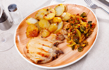 Grilled pork meat with roasted potatoes and braised cabbage served on table.