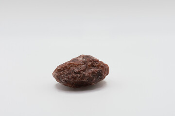 A close up image of an unpolished red calcite crystal on a white background. 