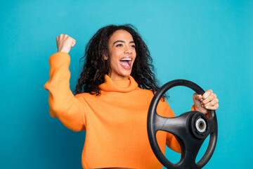 Wall Mural - Portrait of nice young girl hold wheel raise fist wear orange sweater isolated on turquoise color background