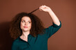 © deagreez - Young woman with curly hair playfully twists her curls against a brown background, wearing a casual green shirt