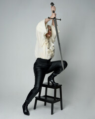 Sticker - Full length portrait of female model wearing vintage gothic fantasy blouse, black leather pants and white blonde plaited hair. holding a sword weapon, action pose,  isolated on studio backdrop.