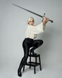 © faestock - Full length portrait of female model wearing vintage gothic fantasy blouse, black leather pants and white blonde plaited hair. holding a sword weapon, action pose,  isolated on studio backdrop.