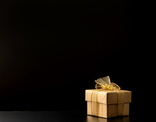 A single, small, golden wrapped gift box sits on a black surface, with a dark background.  generative AI