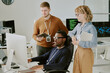 © AnnaStills - Group of three young ethnically diverse IT specialists working together on cybersecurity software in modern office