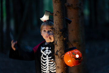 Boy in a forest with Halloween costumes, carved pumpkins with candles and decoration, creepy concept