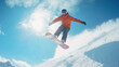 © Jhati - A snowboarder catches air against a sunny mountain backdrop while carving through fresh powder