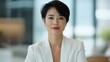 © GenZGraphics - Professional Asian woman wearing a white suit with short hair seated in an office environment