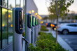 © Vovmar - A row of modern electric vehicle charging stations in front of an office building, with cars parked nearby. Green industry