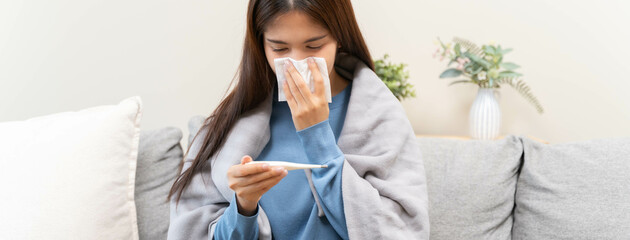 flu in winter season concept, Asian young woman checking her body temperature feeling exhausted from fever at home