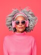 © Anna - Stylish woman with gray hair wearing pink headphones and sunglasses on coral background.