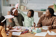 © Seventyfour - African American family enjoying time together while making Easter crafts and decorating eggs at table Children wearing bunny ears and interacting with parents