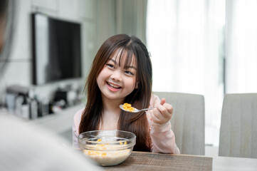 A young, adorable Asian girl is enjoying having breakfast with her mom at a dining table.