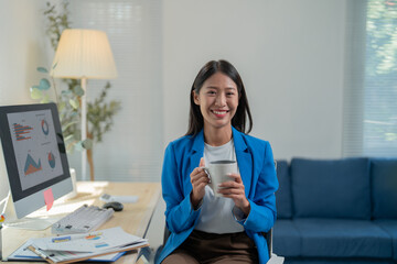 Young asian businesswoman takes a relaxing coffee break at her modern office desk, exuding confidence and success in her career as an entrepreneur