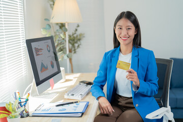 Young asia businesswoman holding credit card and using computer, calculating financial document, working about online payment and holding credit card with smiling face