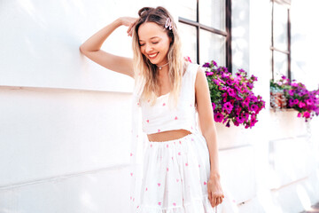 Wall Mural - Young beautiful smiling blond woman in trendy summer top and skirt clothes. Sexy carefree woman posing in street at sunset. Positive model outdoors it sunny day. Cheerful and happy