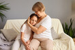 © sementsova321 - Elderly grandmother sitting on comfortable couch at home hugging her upset little granddaughter offering support and love while sad child leaning into her granny