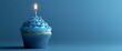 © VINA - A single blue cupcake with a lit candle on top, on a blue background.
