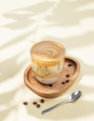 Wall Mural - Iced dalgona coffee. Whipped instant coffee in a glass with ice on a wooden board on a yellow background