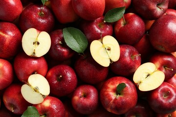 Fresh ripe red apples and green leaves as background, top view