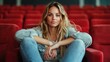© Maximages  - A woman with long hair and casual attire is seated in plush red theater seats, exuding a sense of calm and confidence in this modern indoor setting.