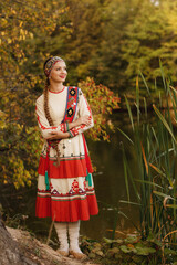 Wall Mural - a girl in a national Chuvash costume by a pond in the autumn forest, filmed in the evening light