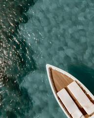 The bow of a yacht sailing in crystal blue waters. The yacht's design is elegant, with striped cushions and wooden details that contrast with the deep blue sea background.