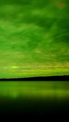 Wall Mural - time lapse of clouds lite green by aurora as they move above a large calm lake.