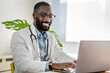 © lordn - Smiling African-American doctor having an online consultation on his laptop in a bright, modern office. He appears engaged, communicating effectively with a patient.