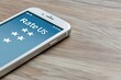 © Hesti - A white smartphone with a blue screen displaying 'Rate Us' with four white stars on a wooden table.