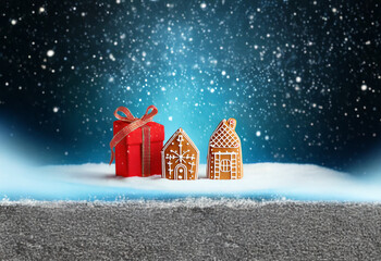 Wall Mural - A red gift box with a ribbon sits in front of two gingerbread houses on a snowy surface under a starry, snowy night sky.