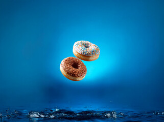 Two donuts, one with chocolate sprinkles and one with white icing and colored sprinkles, are floating against a blue background.