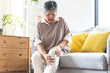 © KMPZZZ - Body arthritis muscles stiff problem, aged woman suffering on leg, pain knee from disease chronic, hand massage rubbing joint injury, mature hurt or sore sitting on sofa at home. Health care people.