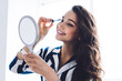 © BullRun - Young happy female looking at mirror and putting mascara