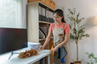 ©  NCST Studio - Young maid wearing an apron is smiling while cleaning an office desk with a feather duster