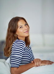 Confident, portrait and woman in home to relax in house for comfort in living room for satisfaction. Smile, calm peace and casual female person in apartment on resting break for wellness in Spain