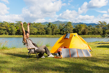 an asian man feeling fresh and happy after sitting and drinking coffee near camping tent beside the 