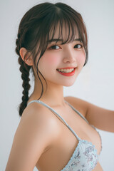 A young Asian woman with Braided Hairstyle poses in a bikini against a white background. Her stylish swimwear and natural beauty are highlighted by the simplicity of the scene.