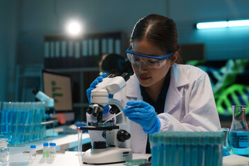 Wall Mural - scientist in a white lab coat and protective glasses is using a microscope and analyzing samples in 