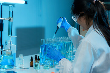 Wall Mural - scientist wearing a lab coat and safety glasses is carefully dropping liquid into a test tube using 