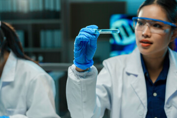 Wall Mural - scientist wearing a lab coat and gloves holding a test tube with blue liquid while working in a labo