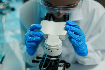 Wall Mural - scientist wearing a lab coat and protective gloves is adjusting a microscope while conducting resear