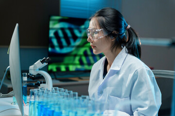 Wall Mural - scientist wearing a lab coat and safety glasses is working on a computer in a laboratory, with test 