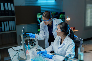 Wall Mural - two female scientists wearing lab coats and safety glasses are working on a computer, analyzing medi