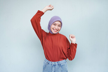 Beautiful young Asian woman in a red sweater raises arms and dances to favorite music, forgot about all problems and looks so happy. isolated over gray background.