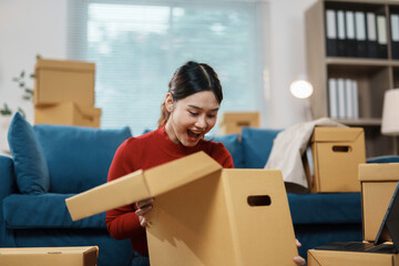 Young woman is unpacking a cardboard box while sitting on the floor of her living room, surrounded by moving boxes