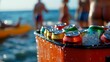 © HambaTuhanImages - A cooler full of aluminum cans sits on a beach with people enjoying a day in the sun.