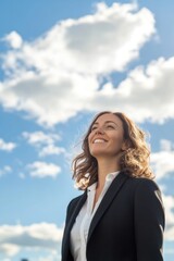 portrait of a businesswoman with medium wavy hair standing while smiling proudly, she is looking at a far, low angle shot, in vertical 2:3 aspect ratio